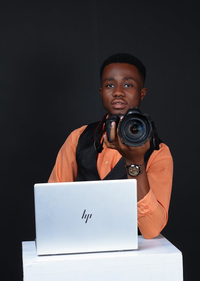 hero-img Portrait of young male photographer holding a camera with a laptop on a table.